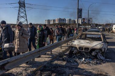 Moradores de Kiev passam por carro queimado; milhões de pessoas fogem do conflito