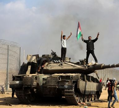 Palestinians wave their national flag and celebrate by a destroyed Israeli tank at the Gaza Strip fence east of Khan Younis southern Saturday, Oct. 7, 2023. The militant Hamas rulers of the Gaza Strip carried out an unprecedented, multi-front attack on Israel at daybreak Saturday, firing thousands of rockets as dozens of Hamas fighters infiltrated the heavily fortified border in several locations by air, land, and sea and catching the country off-guard on a major holiday. (AP Photo/Yousef Masoud)