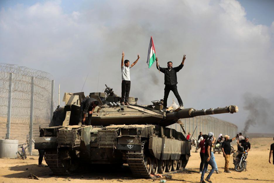 Palestinos agitam comemoram ao lado de um tanque israelense destruído na Faixa de Gaza Foto: Yousef Masoud/AP - 07/10/23