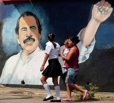 A family walks past a mural depicting Nicaragua's President Daniel Ortega on the wall of a state building in Managua February 10, 2014. Partial reforms to the country's Constitution, approved by the National Assembly in late January, took effect on Monday. Opponents have voiced concern over the reforms, which include removing limits in presidential terms, which they say are likely to allow socialist President Ortega to remain in power indefinitely, according to local media. REUTERS/Oswaldo Rivas (NICARAGUA - Tags: POLITICS)