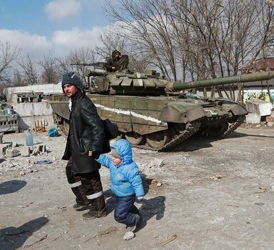 A local resident walks with a child past a tank of pro-Russian troops during Ukraine-Russia conflict in the besieged southern port city of Mariupol, Ukraine March 18, 2022. REUTERS/Alexander Ermochenko