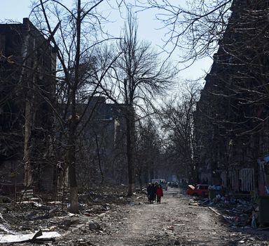 Moradores caminham perto de edifícios residenciais que foram danificados durante bombardeios russos na cidade portuária sitiada de Mariupol, Ucrânia