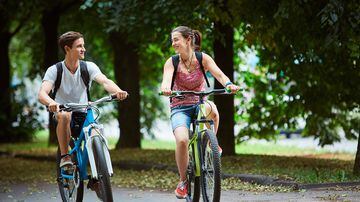 Young people, couple with bicycles in the park. A loving couple on a date on a summer evening. The guy with the girl hugs and kisses. Youth, first feelings, first love, first dates. Foto: vitaliymateha/Adobe Stock       