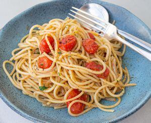 Espaguete, com tomates fatiados em cima, dentro de azul claro. O garfo e a colher estão tombados também dentro do prato