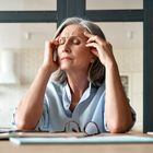Tired stressed old mature business woman suffering from headache at work. Upset sick senior middle aged lady massaging head feeling migraine from overwork or menopause using computer at home office. Foto: insta_photos/Adobe Stock 