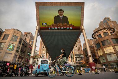 Uma mulher passa de bicicleta por uma grande tela de televisão em um shopping center exibindo a cobertura da televisão estatal chinesa da visita do presidente chinês Xi Jinping a Hong Kong
