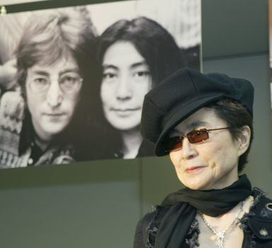 Yoko Ono à frente de foto em que aparece ao lado de John Lennon