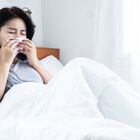 asian woman feeling sick sneezing and have runny nose in bed hand holding tissue paper, allergic to dust mites or flu concept. Foto: doucefleur/Adobe Stock 
