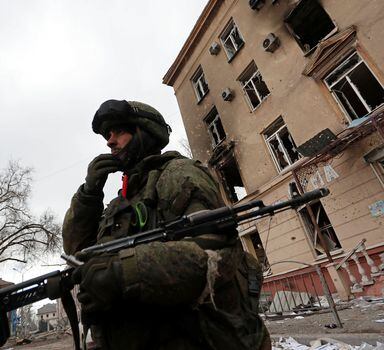 Um membro do serviço de tropas pró-Rússia fica ao lado de um prédio danificado durante o conflito Ucrânia-Rússia na cidade portuária de Mariupol, no sul da Ucrânia, em 3 de abril de 2022