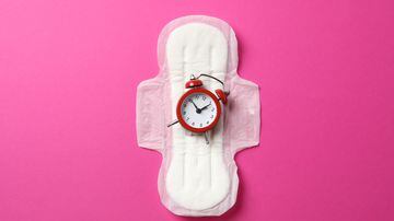 Sanitary pad with alarm clock on pink background, top view. Foto: Atlas/Adobe Stock