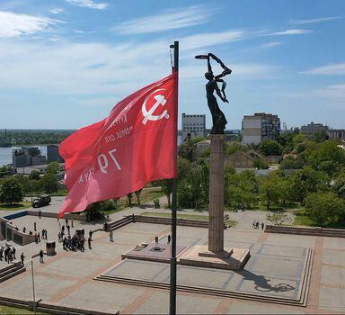 A replica of the Soviet Banner of Victory flies by a WWII memorial in the city of Kherson on May 20, 2022, amid the ongoing Russian military action in Ukraine. - Authorities in the Moscow-controlled Ukrainian region of Kherson announced on May 23 the introduction of the ruble as an official currency alongside the Ukrainian hryvnia. The region's capital Kherson was the first major city to fall to Russian forces after the start of Moscow's military operation in Ukraine on February 24. (Photo by Andrey Borodulin/AFP
