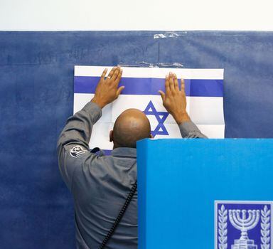 An official adjusts a poster of the Israeli flag at a polling station in Rosh Haayin, Israel, on Tuesday, Sept. 17, 2109. MUST CREDIT: Bloomberg photo by Kobi Wolf.