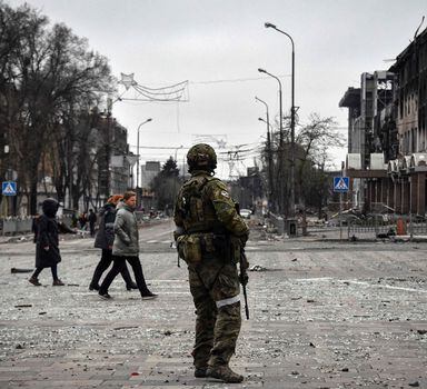 TOPSHOT - People pass by a Russian soldier in central Mariupol on April 12, 2022, as Russian troops intensify a campaign to take the strategic port city, part of an anticipated massive onslaught across eastern Ukraine, while Russia's President makes a defiant case for the war on Russia's neighbour. - *EDITOR'S NOTE: This picture was taken during a trip organized by the Russian military.* (Photo by Alexander NEMENOV / AFP)