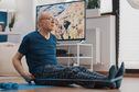 Aged man using resistance band to stretch arms and legs on yoga mat. Elder person pulling flexible elastic belt, stretching muscles and doing fitness exercise. Senior adult training