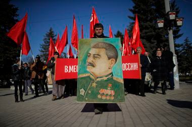 Simpatizantes marcham com bandeiras soviéticas e a foto do ditador Josef Stalin em sua cidade natal de Gori, na Geórgia