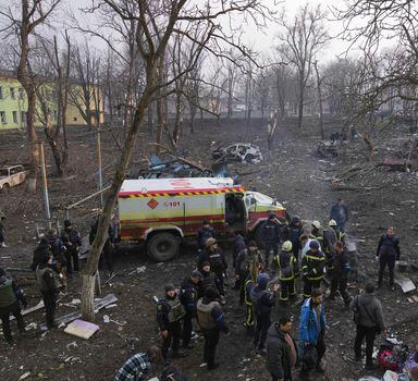 Ukrainian servicemen and firefighters stand in the area outside of a maternity hospital damaged in a shelling attack in Mariupol, Ukraine, Wednesday, March 9, 2022. Associated Press journalists, who have been reporting from inside blockaded Mariupol since early in the war, documented this attack on the hospital and saw the victims and damage firsthand. They shot video and photos of several bloodstained, pregnant mothers fleeing the blown-out maternity ward, medics shouting, children crying. (AP Photo/Evgeniy Maloletka)
