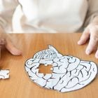 Elderly woman hands putting missing white jigsaw puzzle piece down into the place as a human brain shape. Creative idea for memory loss, dementia, Alzheimer's disease and mental health concept. Foto: Orawan/Adobe Stock 