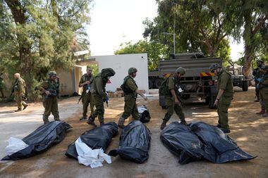Soldados israelenses ao lado de corpos mortos por terroristas do Hamas no kibutz Kfar Azza.