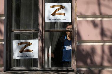 Mulher observa através de janelas marcadas com cartazes da letra Z, que se tornou símbolo da Rússia na guerra da Ucrânia, em imagem do sábado, 21. Hashtag afirma: "Não vamos abandonar os nossos"