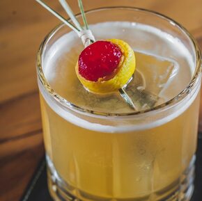 Drinque de uísque com amaretto em copo baixo transparente e enfeitado com uma cereja e uma casca de limão siciliano. Foto: Elvis Fernandes/Divulgação