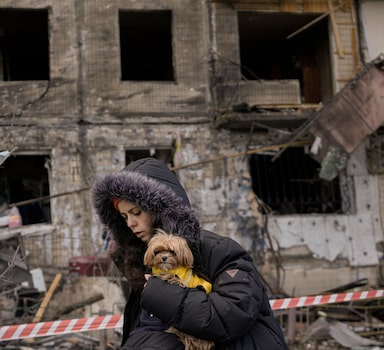 Mulher carregando seu cachorro caminha em frente a um prédio residencial em Kiev destruído por bombardeio russo