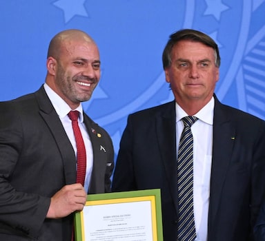 Brazilian President Jair Bolsonaro (R) and deputy Daniel Silveira, pose with a framed copy of the presidential pardon, during an act in defense of freedom of expression at Planalto Palace in Brasilia on April 27, 2022. - Brazilian President Jair Bolsonaro defended his decision to grant a pardon to a controversial ally convicted of attacking democratic institutions, saying "I free people who are innocent." The far-right president has come in for criticism since pardoning Congressman Daniel Silveira, a day after the Supreme Court sentenced the 39-year-old lawmaker to eight years and nine months in prison for his role leading a movement calling for the court to be overthrown. (Photo by EVARISTO SA / AFP)
