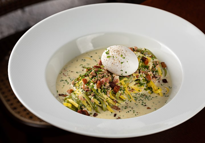 Massa uova pepenara servido em um prato fundo branco, com generoso pedaço de mussarela de búfala em cima. O prato está sobre uma mesa de madeira.