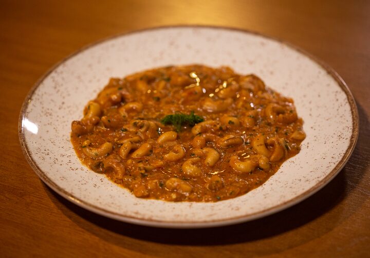 Strogonoff vegano, com cogumelos e castanhas, servido em um prato raso de cor bege, com borda e detalhes dourados. O prato está sobre uma mesa de madeira.