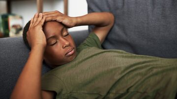 Side view of sick african american boy kid lying on couch in his room with closed eyes holding head in hands, suffering from headache or migraine after stressful hard day at school. Foto: Anatoliy Karlyuk/Adobe Stock 