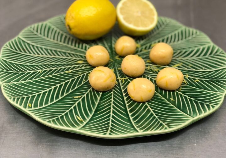 Prato em formato de folha com 7 bolinhas de brigadeiro de limão siciliano com limões sicilianos fatiado e inteiro ao fundo