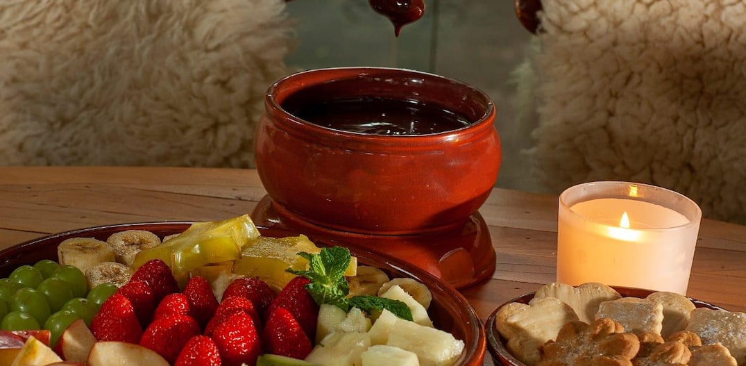 Um prato de frutas variadas e biscoitos acompanha um fondue de chocolate em panela própria para o preparo. Foto: Renan Alves/Divulgação