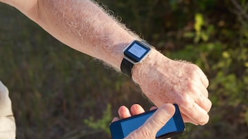 Senior man checking his heart rate and step count outdoor using his smart watch and smartphone; grass in the background. Foto: Lana/Adobe Stock