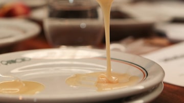 Uma mão segura colher de plástico transparente com uma porção de leite condensado que escorre sobre um prato branco. Foto: FELIPE RAU