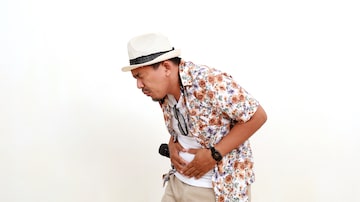 Painful asian adult man tourist standing while holding his stomach. Suffering from stomach ache. Concept of travel. Isolated on white background. Foto: Adobe Stock
