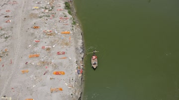 Homem navega pelo Ganges diante de vários corpos sepultados na areia; autoridades suspeitam que sejam de vítimas de coronavírus. Foto: Ritesh Shukla/Reuters
