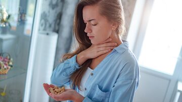 Young sick upset woman suffers from choking and cough from allergic reaction from peanut. Danger of nuts food allergy. Foto: Goffkein/Adobe Stock