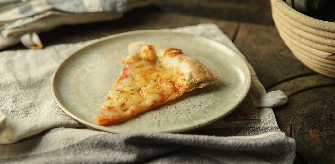 Prato acinzentado com uma fatia de pizza, sob o prato, tecido cinza. Foto: DANIEL TEIXEIRA