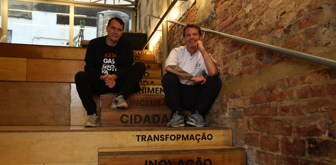 Dois homens sentados em uma escada de madeira com os dizeres: transformação, inovação e dignidade. Foto: EdipoFerraz
