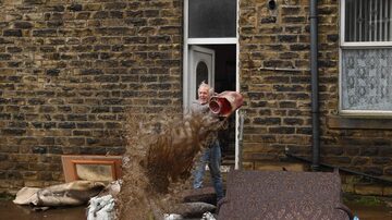 Homem usa um balde para retirar água de dentro de imóvel emMytholmroyd, no norte da Inglaterra. Foto: Oli SCARFF / AFP