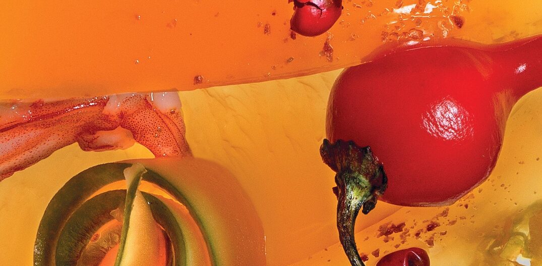 A imagem mostra fragmentos de uma geleia de crustáceos na cor alaranjada, com destaque para uma pimenta biquinho vermelha. Foto: Sérgio Coimbra