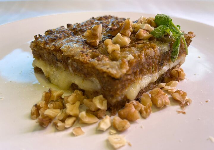 Em um prato de louça branca, uma porção de quibe de abóbora recheado com queijo mussarela e parmesão, com nozes picadas e folhas de hortelã por cima.