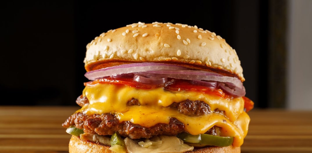 Burger day deluxe do Jurassic Park com dois discos de carne bovina, duas camadas de queijo, pepperoni, cogumelos, pimentão verde, azeitona e cebola roxa. Foto: Rubens Kato