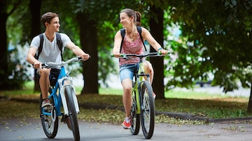 Young people, couple with bicycles in the park. A loving couple on a date on a summer evening. The guy with the girl hugs and kisses. Youth, first feelings, first love, first dates. Foto: vitaliymateha/Adobe Stock       