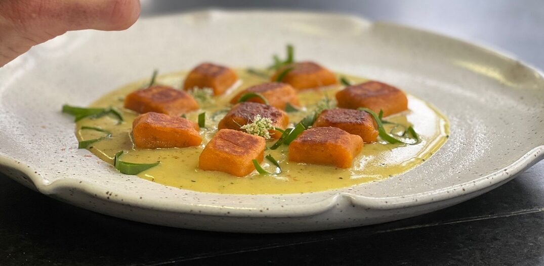Prato branco com pedaços de alimento laranja com molho amarelado de pequi cobrindo o fundo. Foto: Le Cordon Bleu | Deni Bloch