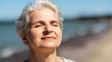 people and leisure concept - portrait of happy senior woman enjoying sun on beach. Foto: Syda Productions/Adobe Stock