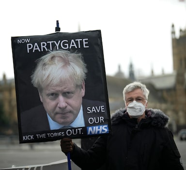 FILE - An anti-Conservative Party protester holds a placard with an image of British Prime Minister Boris Johnson including the words "Now Partygate" backdropped by the Houses of Parliament, in London, Wednesday, Dec. 8, 2021. British police are getting ready to issue a first batch of fines on over parties held by Prime Minister Boris Johnsonâ€™s staff during coronavirus lockdowns. The Metropolitan Police declined to confirm reports multiple U.K. media outlets that fines would come as soon as Tuesday, March 29, 2022, saying it would not give â€œa running commentaryâ€ on its probe. (AP Photo/Matt Dunham, File)