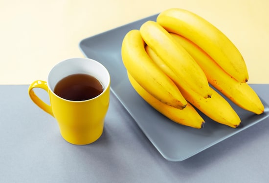 Cacho de banana ao lado de caneca amarela com chá dentro. Foto: Viktoriya | Adobe Stock