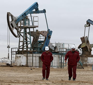 FILE PHOTO: Workers walk as oil pumps are seen in the background in the Uzen oil and gas field in the Mangistau Region of Kazakhstan November 13, 2021. REUTERS/Pavel Mikheyev/File Photo