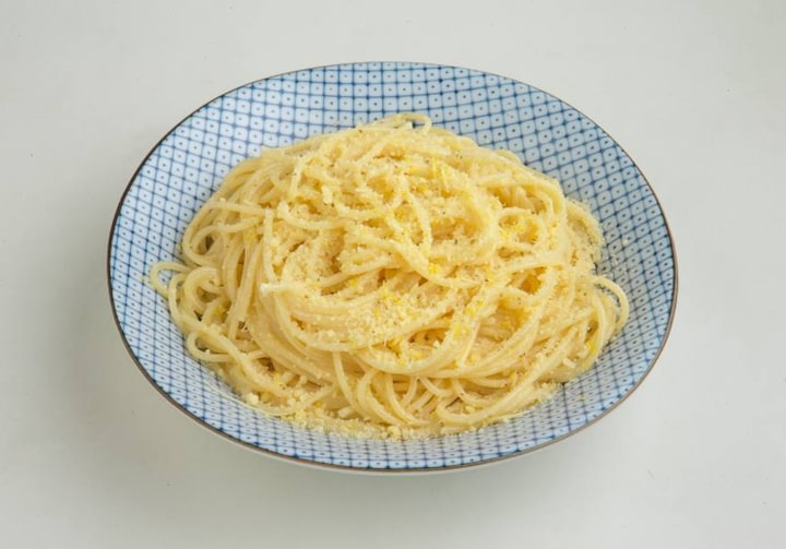 Prato quadriculado azul e branco, com espaguete ao limão, sobre superfície branca.