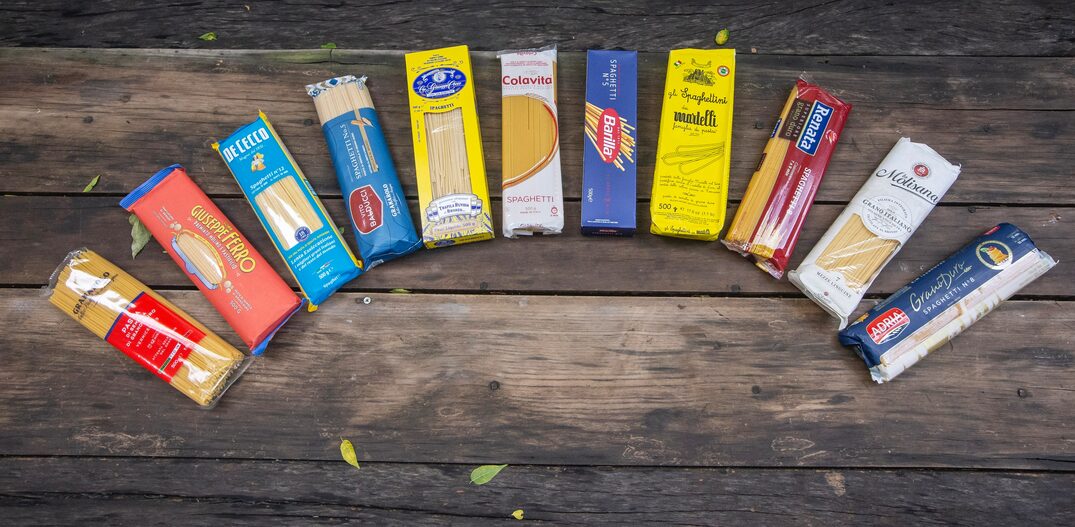 10 embalagens de espaguete de marcas variadas sobre fundo de madeira. Foto: Taba Benedicto/Estadão